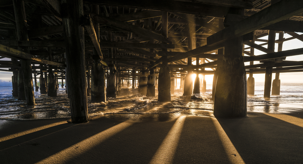 Beautiful San Diego Photoshoot location Under Pacific Beach Pier with sunset beam rays shining through pier pillars. San Diego, California