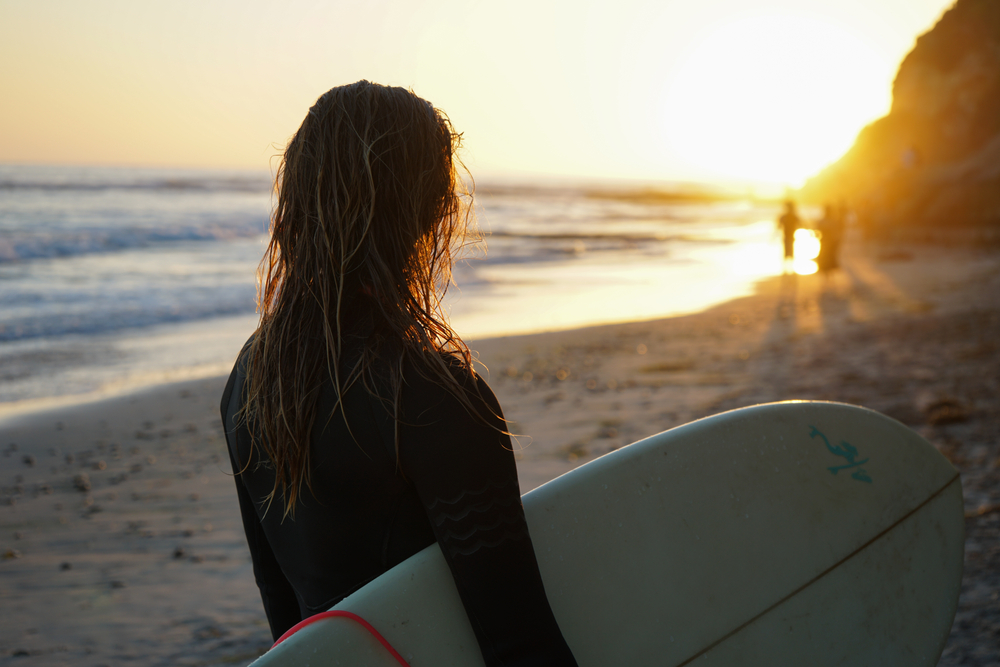 person staring off into the sunset while holding a surfboard